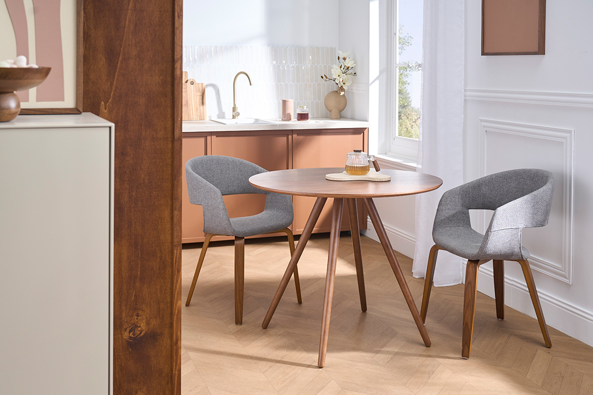 Sedie di design grigie in tessuto con gambe in legno scuro attorno a un tavolo rotondo in un interno moderno.