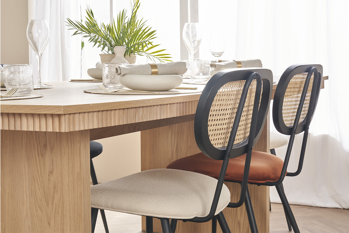 Sedie in velluto terra bruciata e rattan, intorno a un tavolo in legno chiaro.
