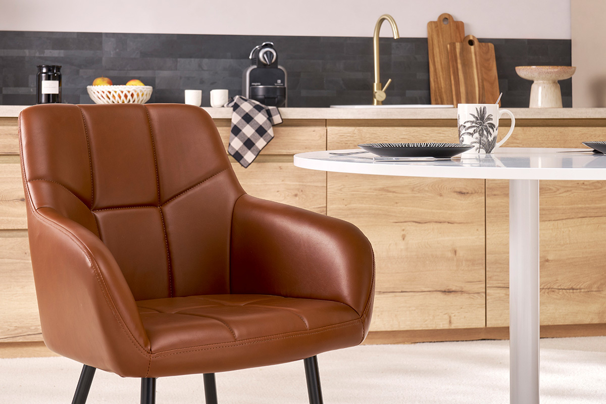 Sedia imbottita marrone MONTERO di fronte a un tavolo rotondo bianco.