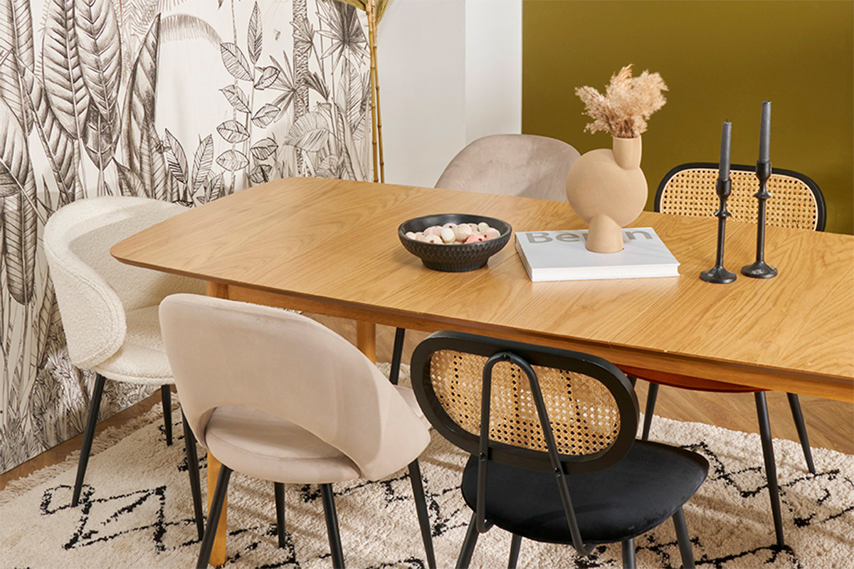 Sedie design in velluto e rattan intorno a un tavolo in legno chiaro.