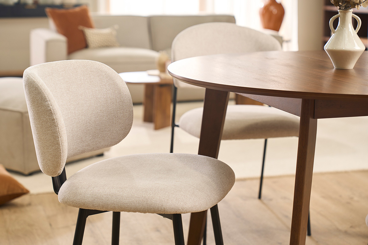 Sedie beige in tessuto con basamento in metallo nero intorno a un tavolo in legno, vista parziale.