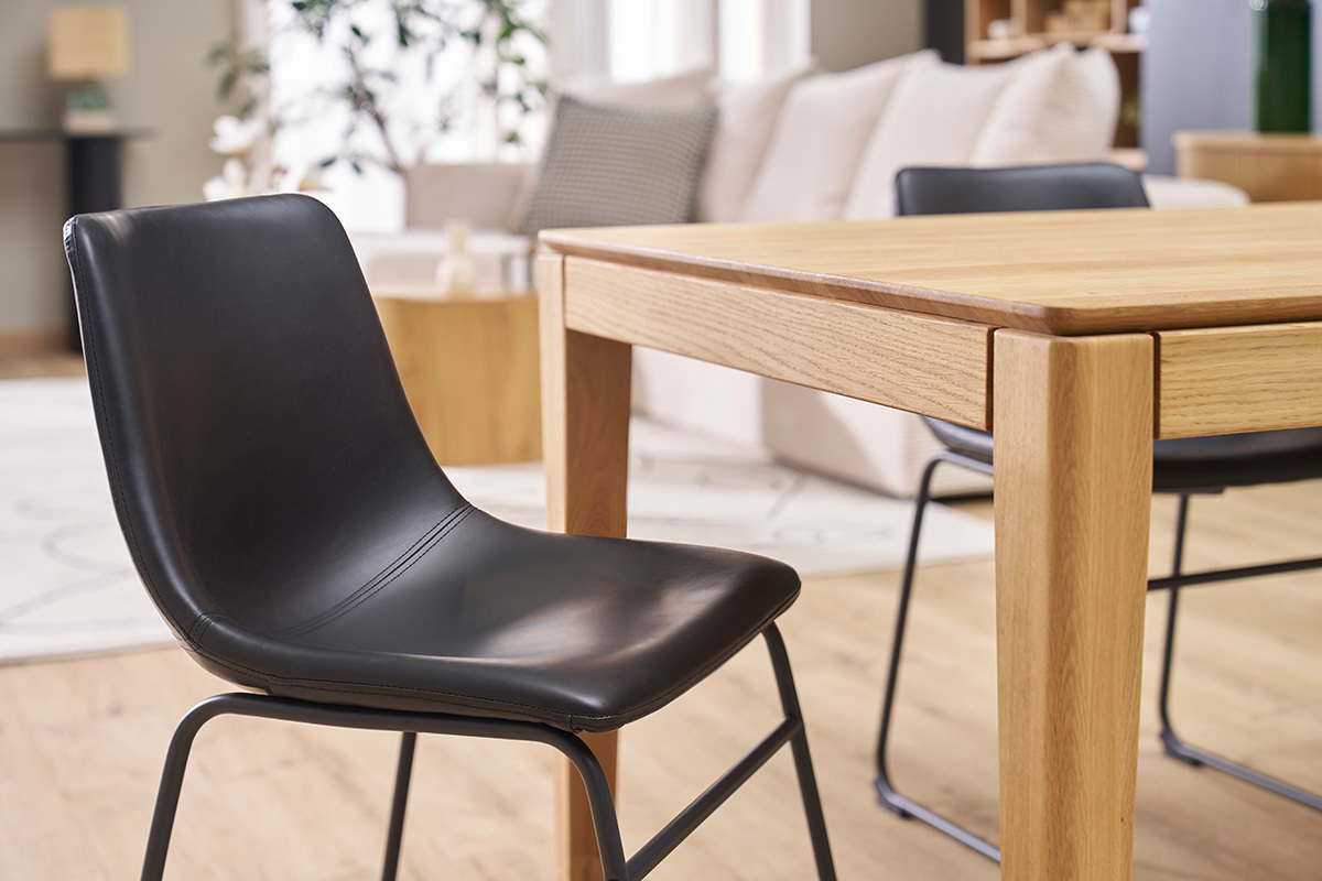 Sedia industriale nera NEW ROCK davanti a un tavolo in legno in un interni moderno.