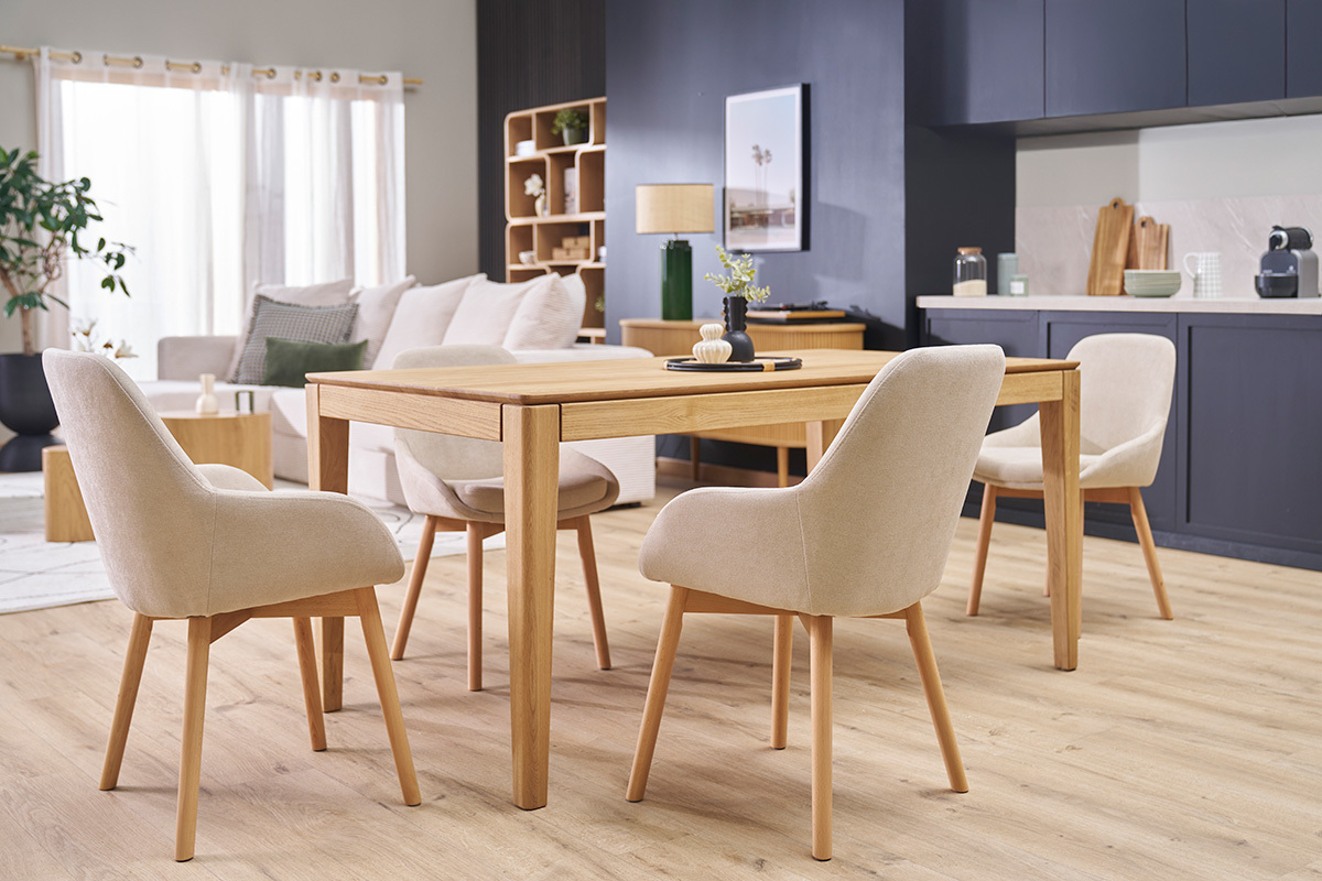 Sedie scandinave in tessuto beige e legno chiaro intorno a un tavolo in legno.