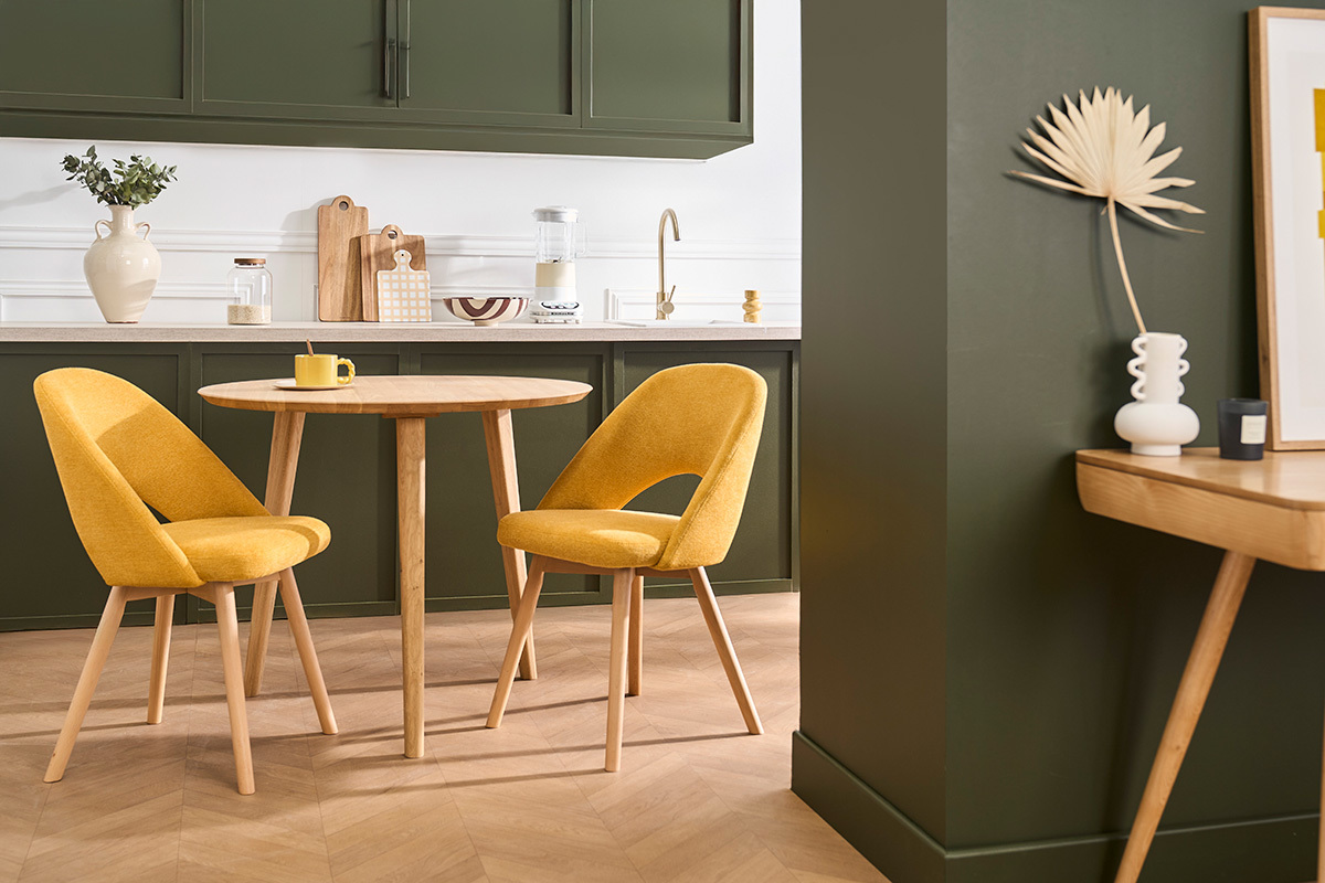 Due sedie scandinave in tessuto giallo senape e legno chiaro intorno a un tavolo rotondo in legno.