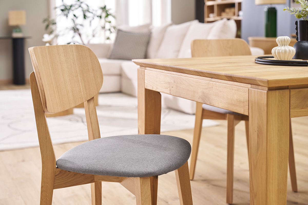 Sedia vintage in legno chiaro con seduta in tessuto grigio chiaro davanti a un tavolo in legno.