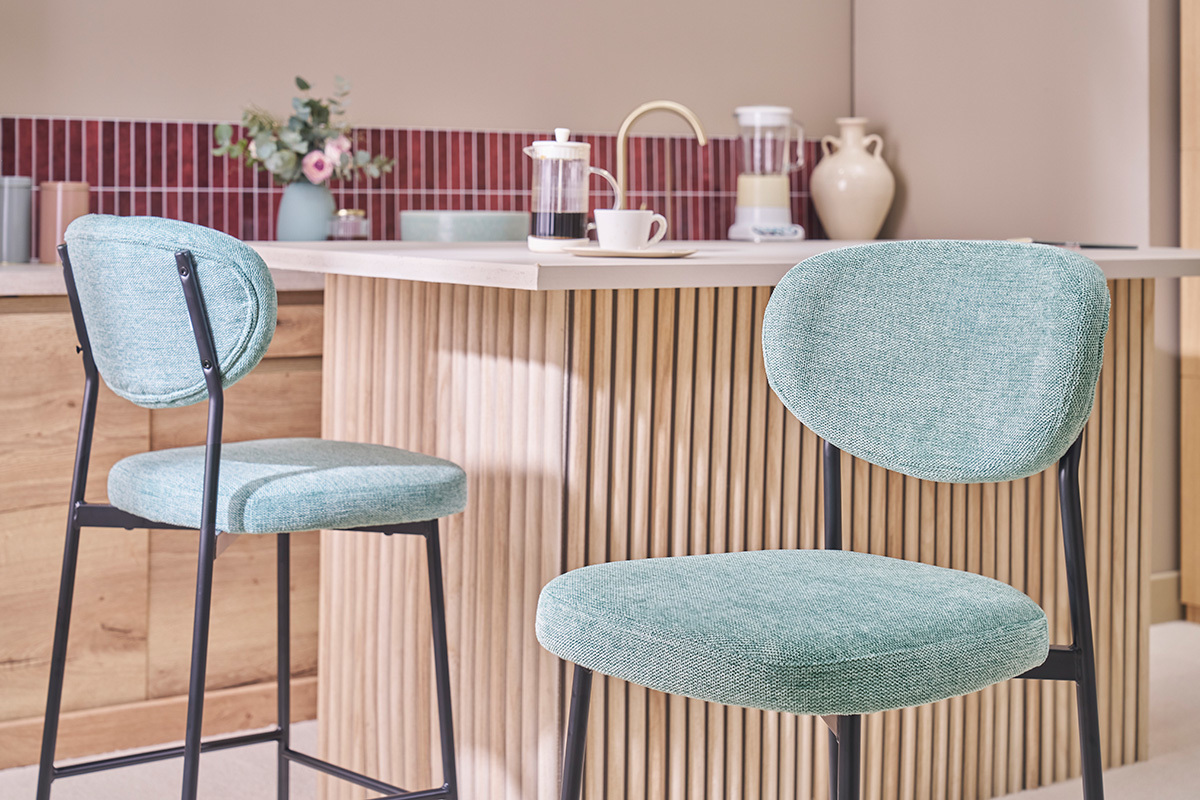 Due sgabelli da bar in tessuto celadon e metallo nero davanti a un'isola da cucina.