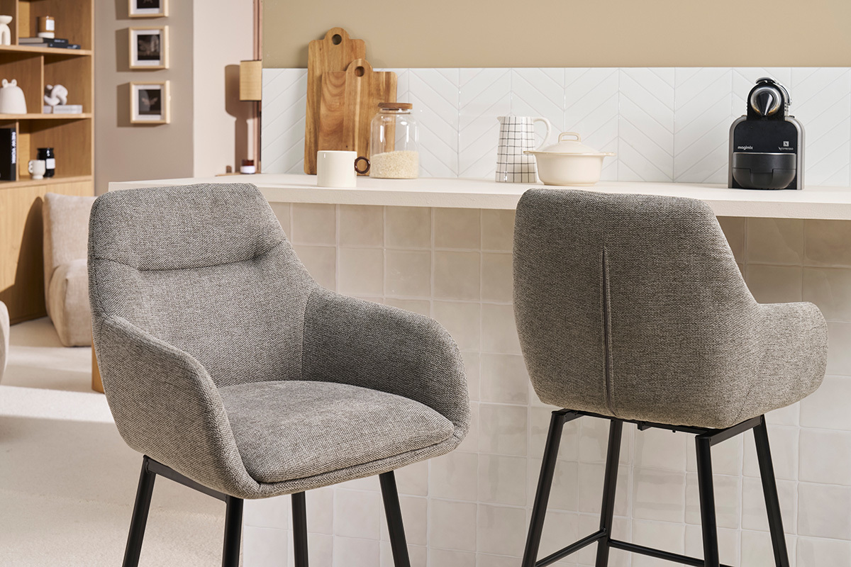 Due sedie da bar grigie in tessuto viste di profilo e di schiena davanti a un bancone.