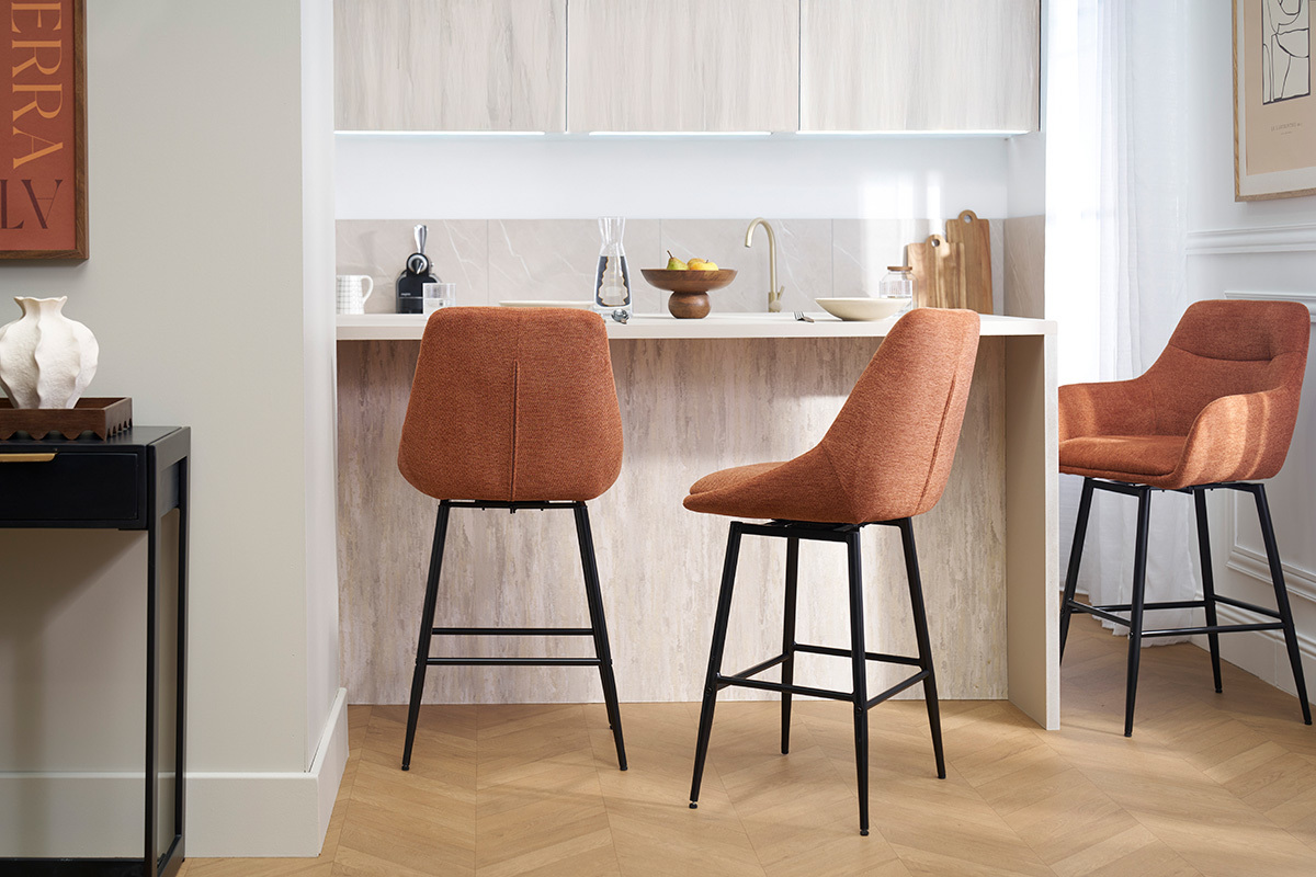 Tre sgabelli da bar ALESS in tessuto terra bruciata e metallo intorno a un bancone da cucina.