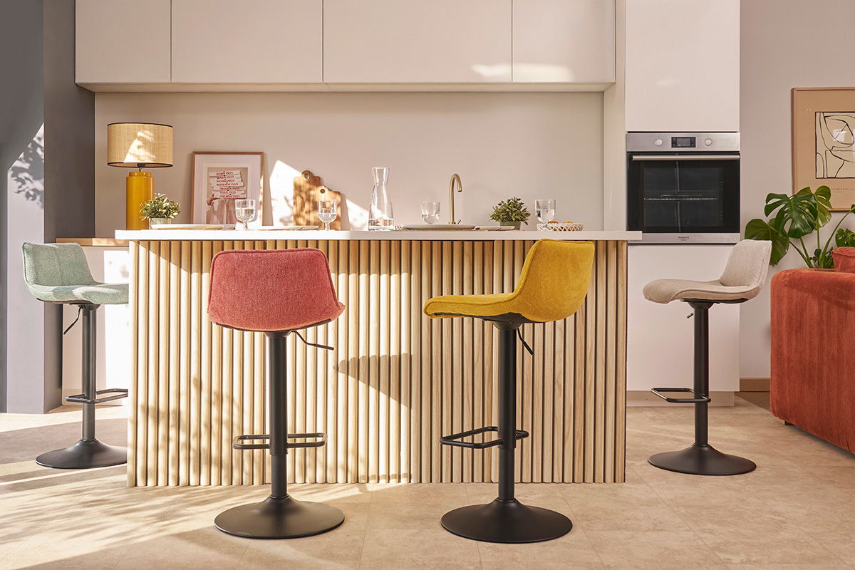 Quattro sgabelli da bar colorati intorno a un'isola da cucina in legno e bianco, interni moderni.