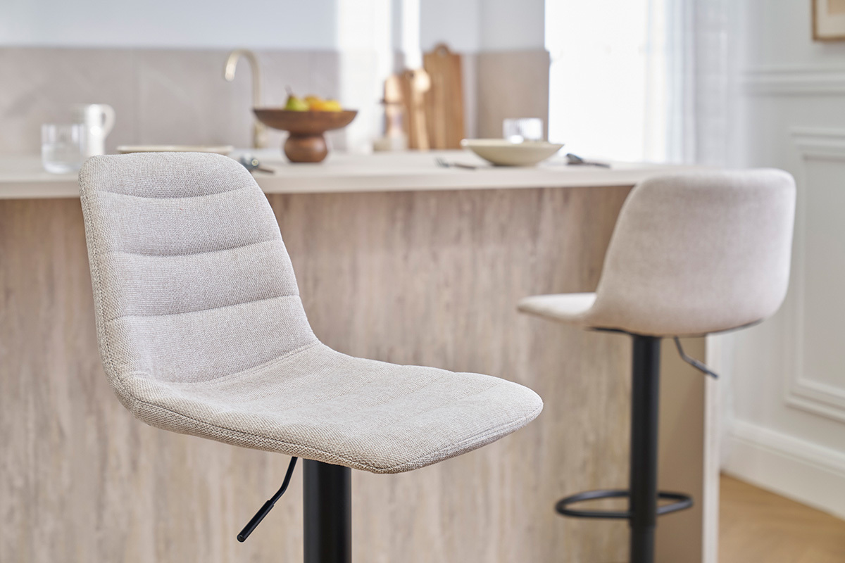 Sgabelli da bar regolabili in tessuto beige e metallo nero davanti a un bancone.