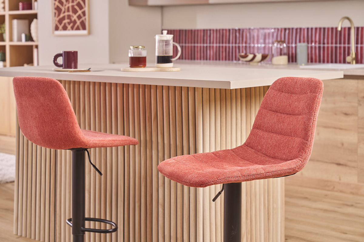 Due sgabelli da bar in tessuto terracotta con gambe in metallo nero davanti a un'isola da cucina.