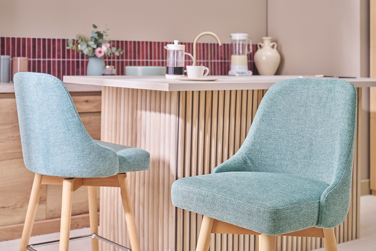 Sgabelli da bar verdi celadon in tessuto e legno, davanti a un bancone moderno.