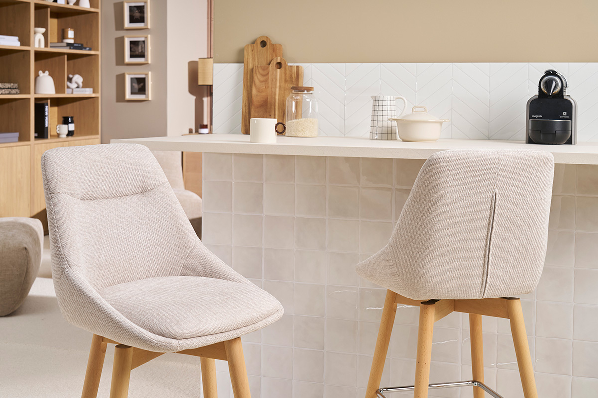 Due sgabelli da bar scandinavi in tessuto beige e legno chiaro davanti a un bancone da cucina.