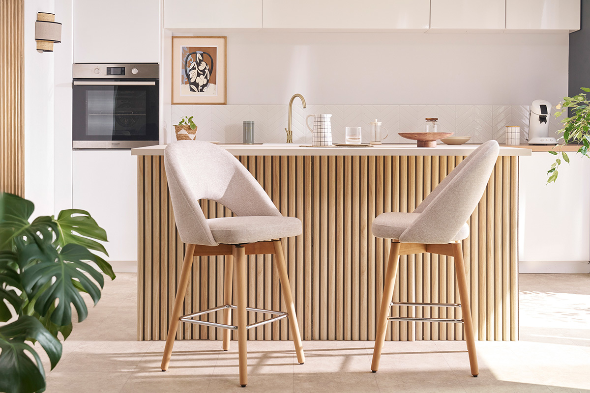 Sgabelli da bar beige in tessuto con gambe in legno massello di hevea davanti a un bancone da cucina.