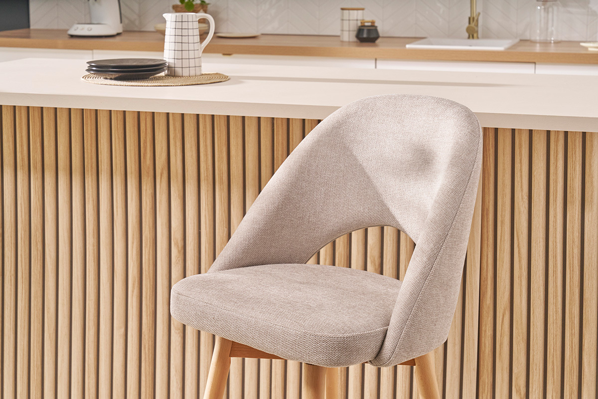 Sgabello da bar scandinavo in tessuto beige e legno massello di hevea davanti a un bancone in legno.