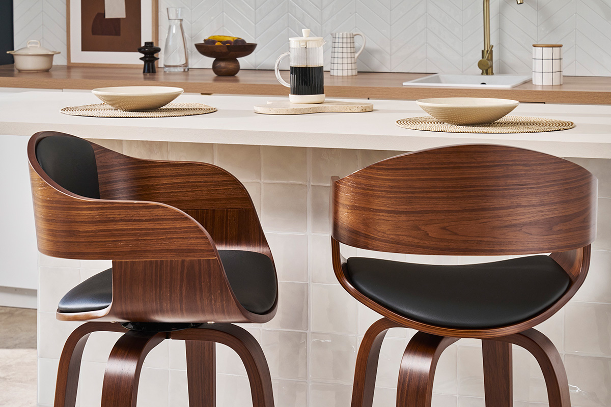 Due sgabelli da bar in legno scuro con sedili neri davanti a un bancone, vista di lato.