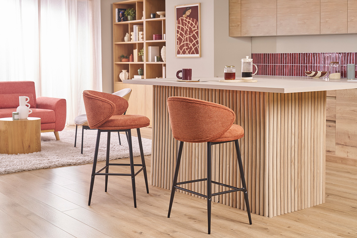Sgabelli da bar in tessuto terracotta e metallo nero davanti a un'isola centrale in legno.