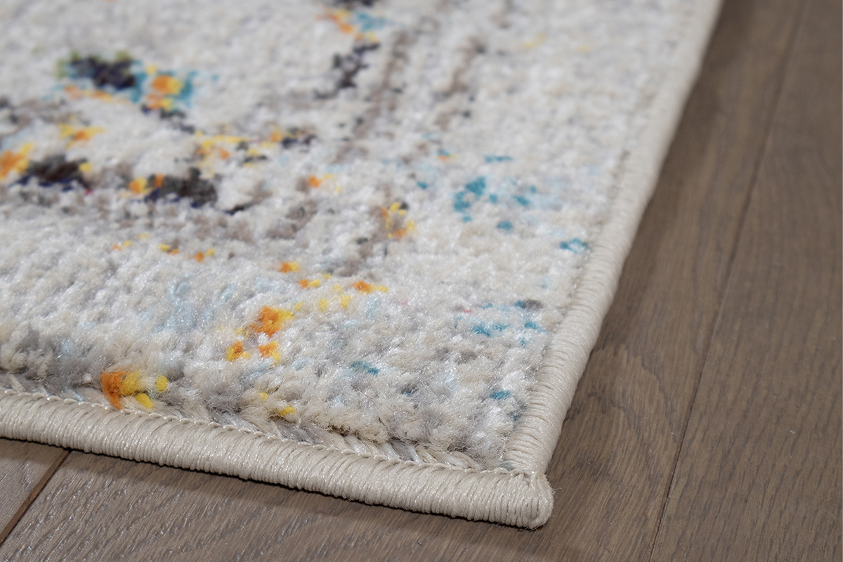 Tappeto rettangolare DULCE multicolore, vista ravvicinata sul motivo e bordo su pavimento in legno.