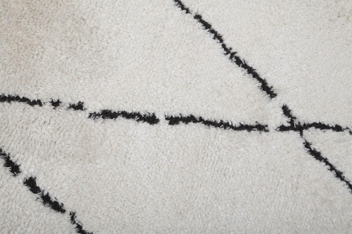 Primo piano su un tappeto con motivi a diamanti neri su sfondo avorio.