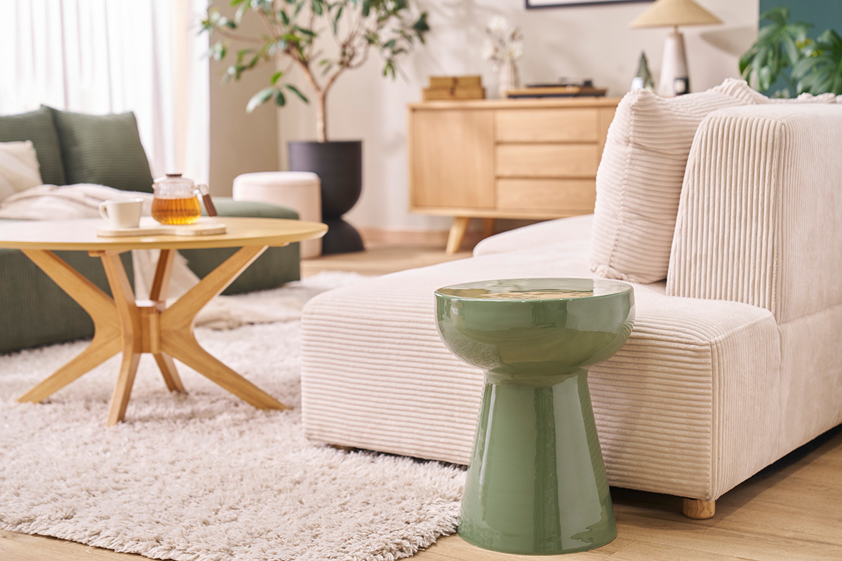 Tavolino rotondo in metallo smaltato verde kaki accanto a un divano beige, vista ingrandita.