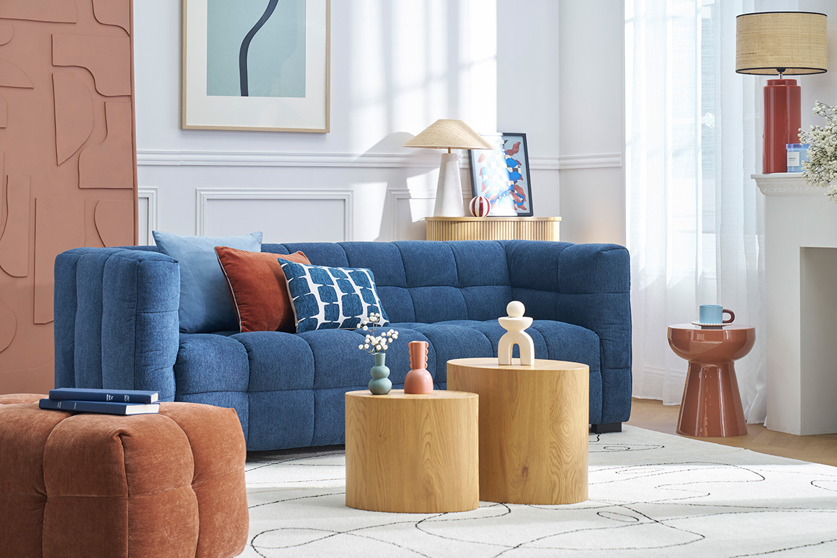 Salone con divano blu, cuscini colorati, tavolino rotondo terracotta sulla destra.