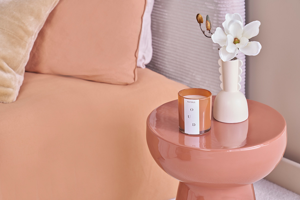 Tavolino MOGOU terracotta con candela e vaso vicino a un letto.