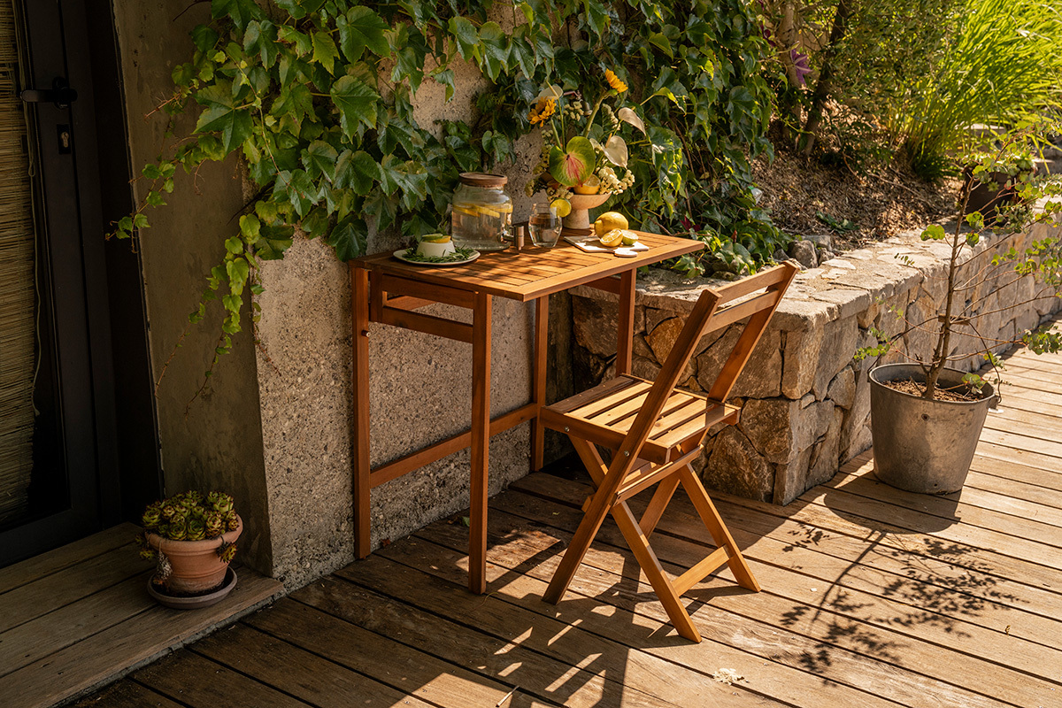 Tavolo da balcone pieghevole in legno massello L80 cm, vista a 3/4 con sedia e decorazioni su un balcone