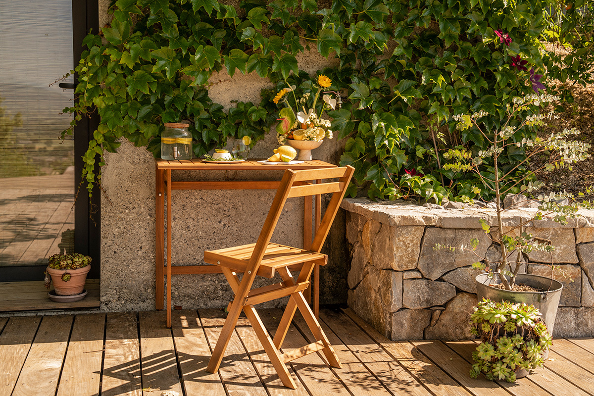 Tavolo da balcone pieghevole in legno massiccio, vista frontale con piante e una sedia in legno