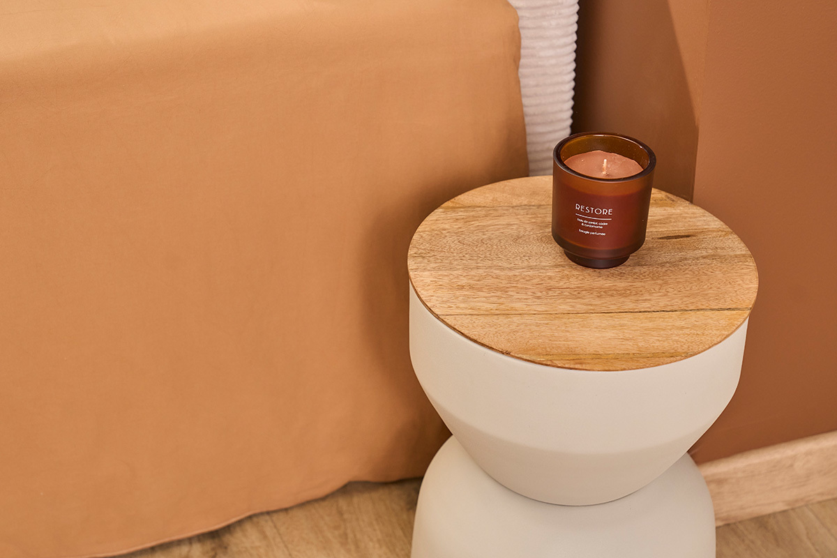 Tavolino rotondo in metallo color greige con piano in legno e candela, vista dall'alto.