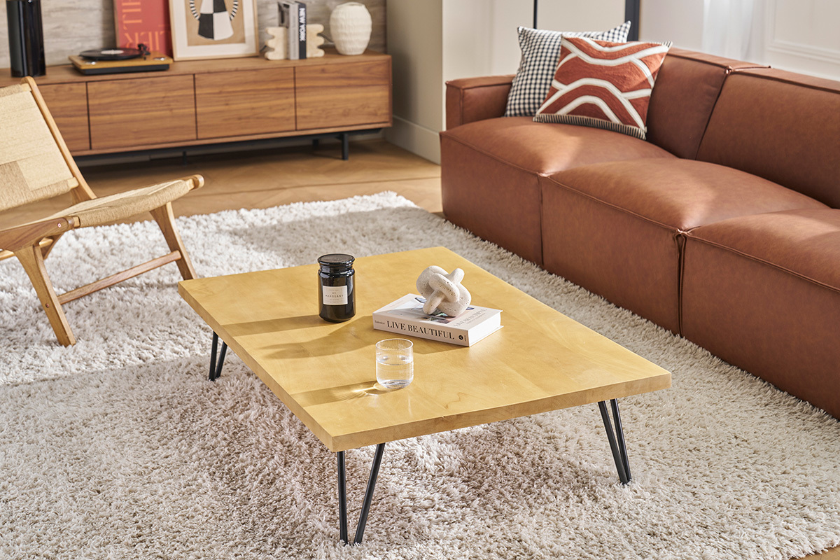 Tavolino basso VIBES in legno di mango e metallo, vista a tre quarti, in un soggiorno con divano e poltrona.