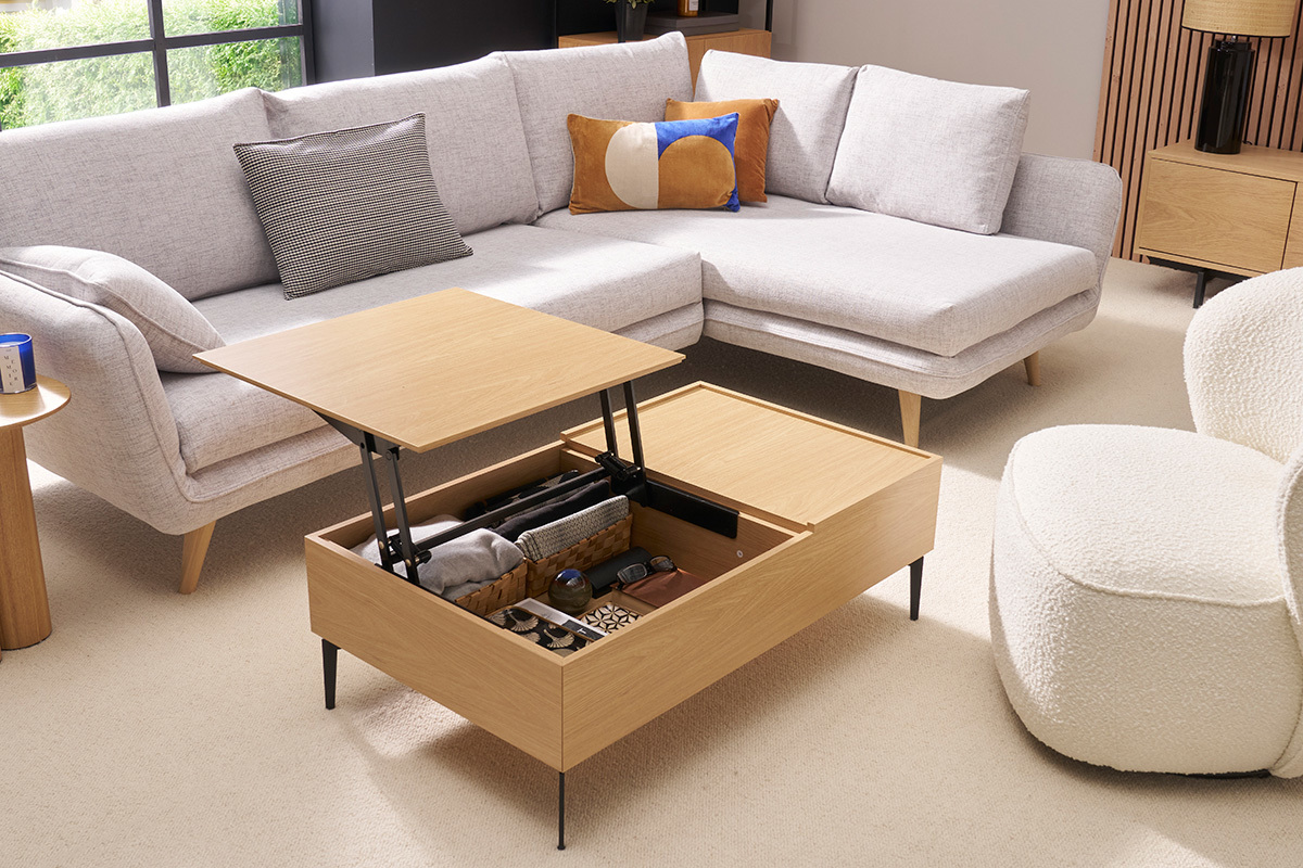 Tavolino sollevabile in legno chiaro con piano apribile, ripostigli visibili, in un salotto moderno.