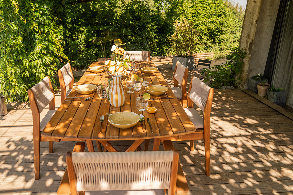 Tavolo da giardino allungabile in legno massello, vista laterale con stoviglie, pronto per un pasto all'aperto.