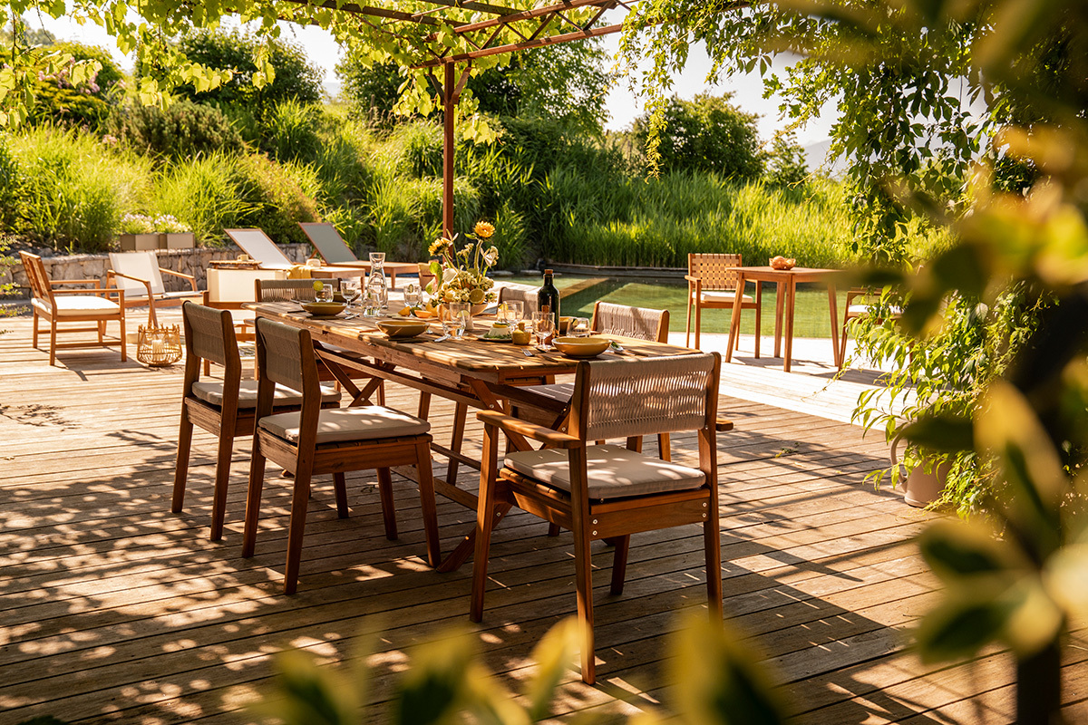 Tavolo da giardino allungabile in legno massiccio con sedie, vista parziale su una terrazza soleggiata