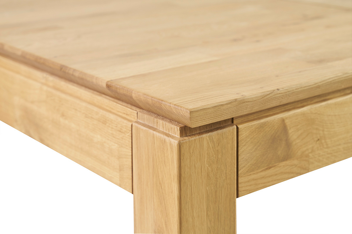 Dettaglio d'angolo di un tavolo da pranzo in legno chiaro, piano e piede visibili.