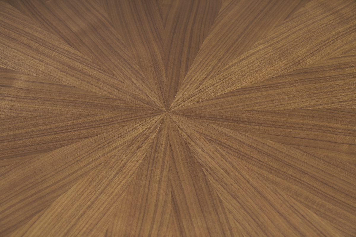 Piano di un tavolo rotondo in impiallacciatura di noce con motivo a sole visto da vicino.