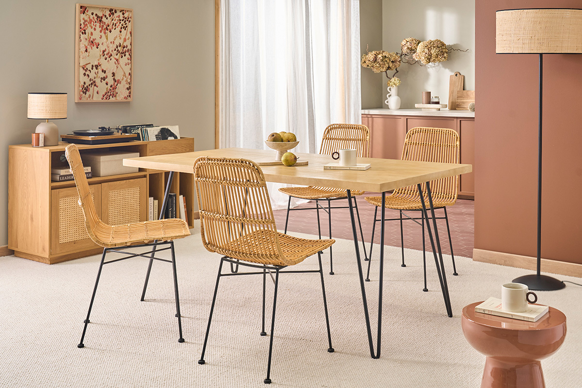 Tavolo da pranzo in legno con gambe in metallo nero, circondato da sedie in rattan, vista da tre quarti.