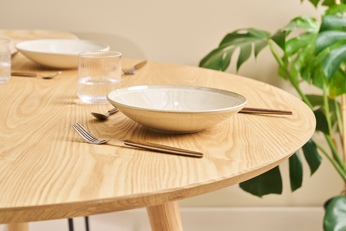 Tavolo rotondo in quercia massiccio con posate e piatto, vista ravvicinata.