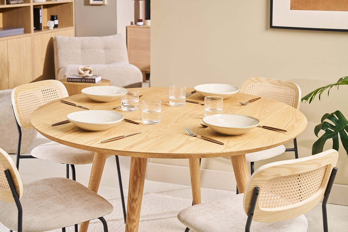 Tavolo da pranzo rotondo in legno chiaro con stoviglie, vista d'insieme.