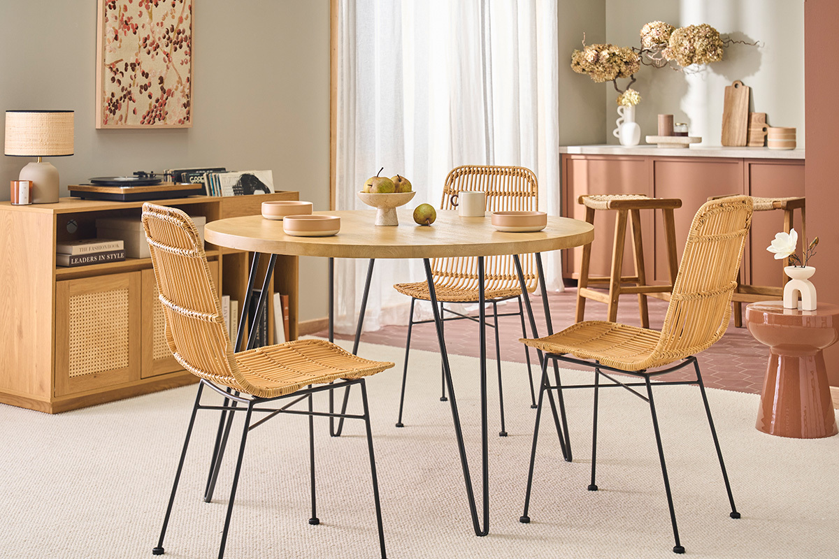 Tavolo rotondo in legno con gambe in metallo, circondato da sedie in vimini, in un interno moderno.